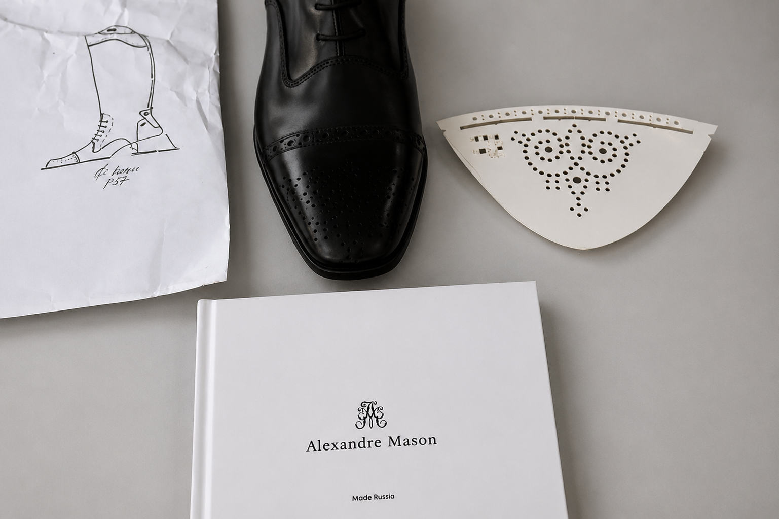 Design development flat lay with a riding boot sketch, black leather sample, perforated pattern and Alexandre Mason book