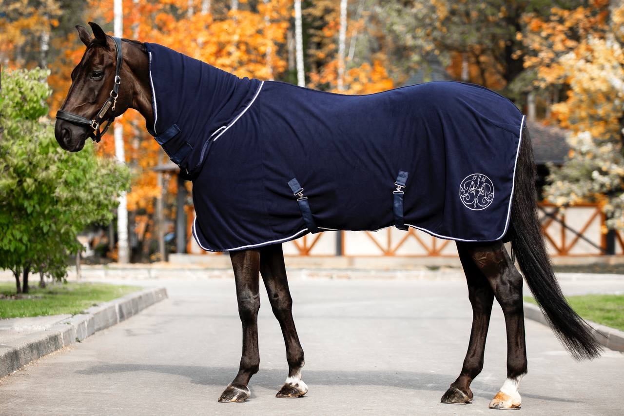 Dark bay horse wearing a navy fleece rug with white piping and embroidered monogram
