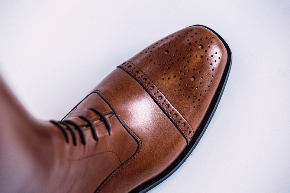 Toe cap of a cognac laced riding boot with fine brogue perforation