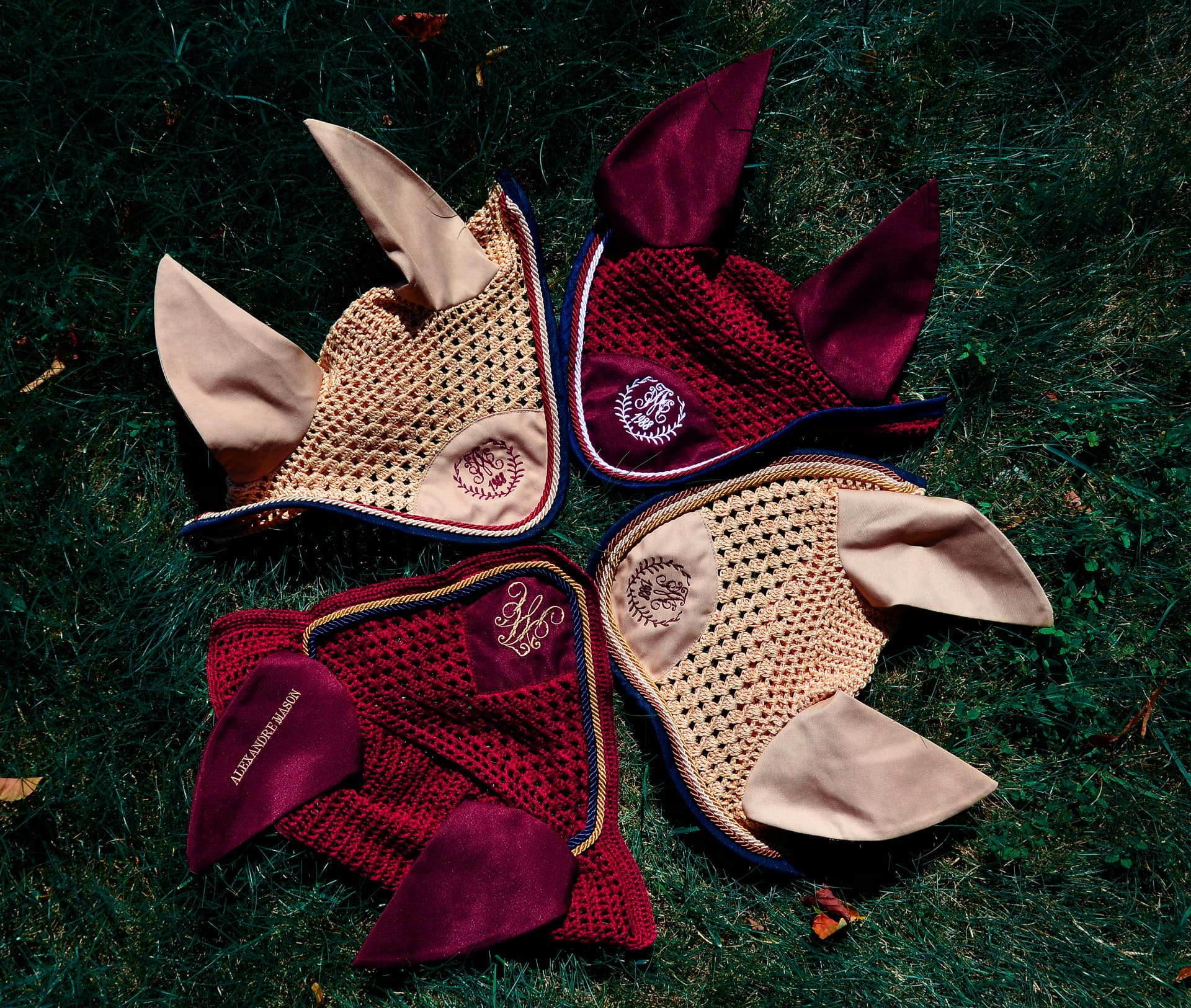 Four crocheted fly bonnets with monogrammed embroidery arranged on grass