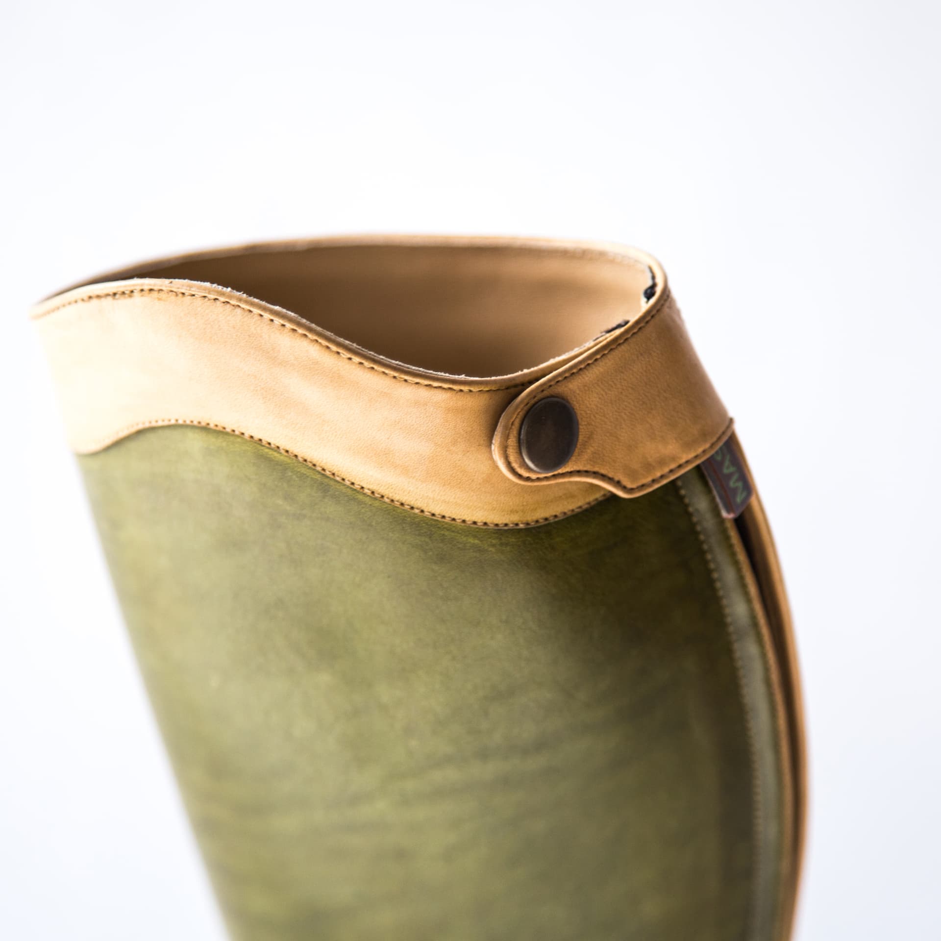Detail of a natural leather cuff with snap button on an olive green boot