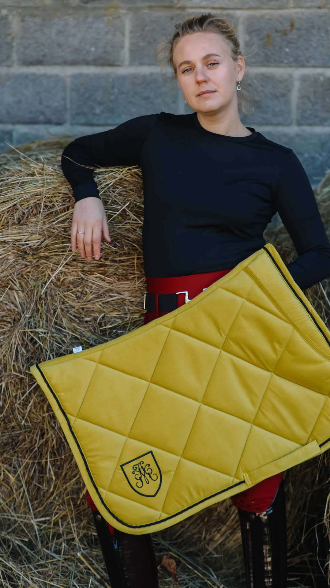 Rider holding a mustard quilted saddle pad with monogrammed crest