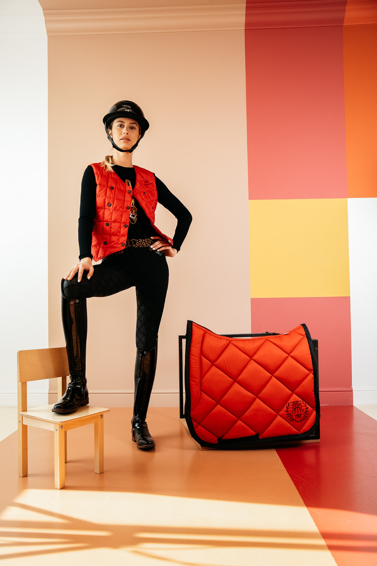 Rider in a red quilted gilet and patent dressage boots beside a matching red quilted saddle pad