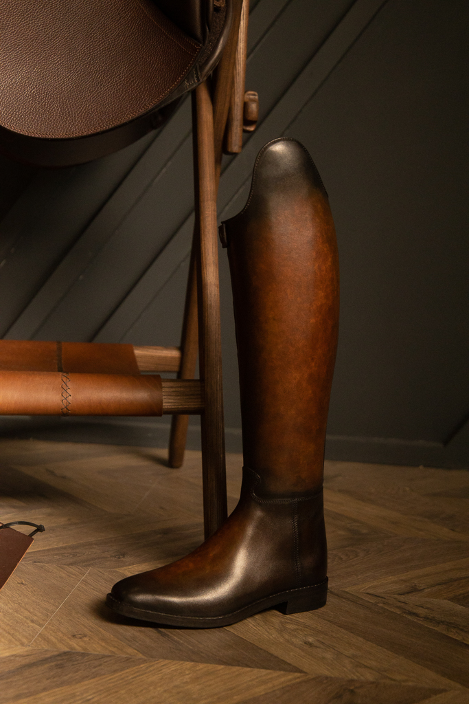 Hand-patinated brown dressage boot standing on herringbone parquet
