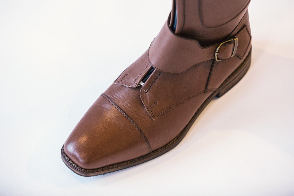 Detail of a brown leather boot with brass buckle and side zip