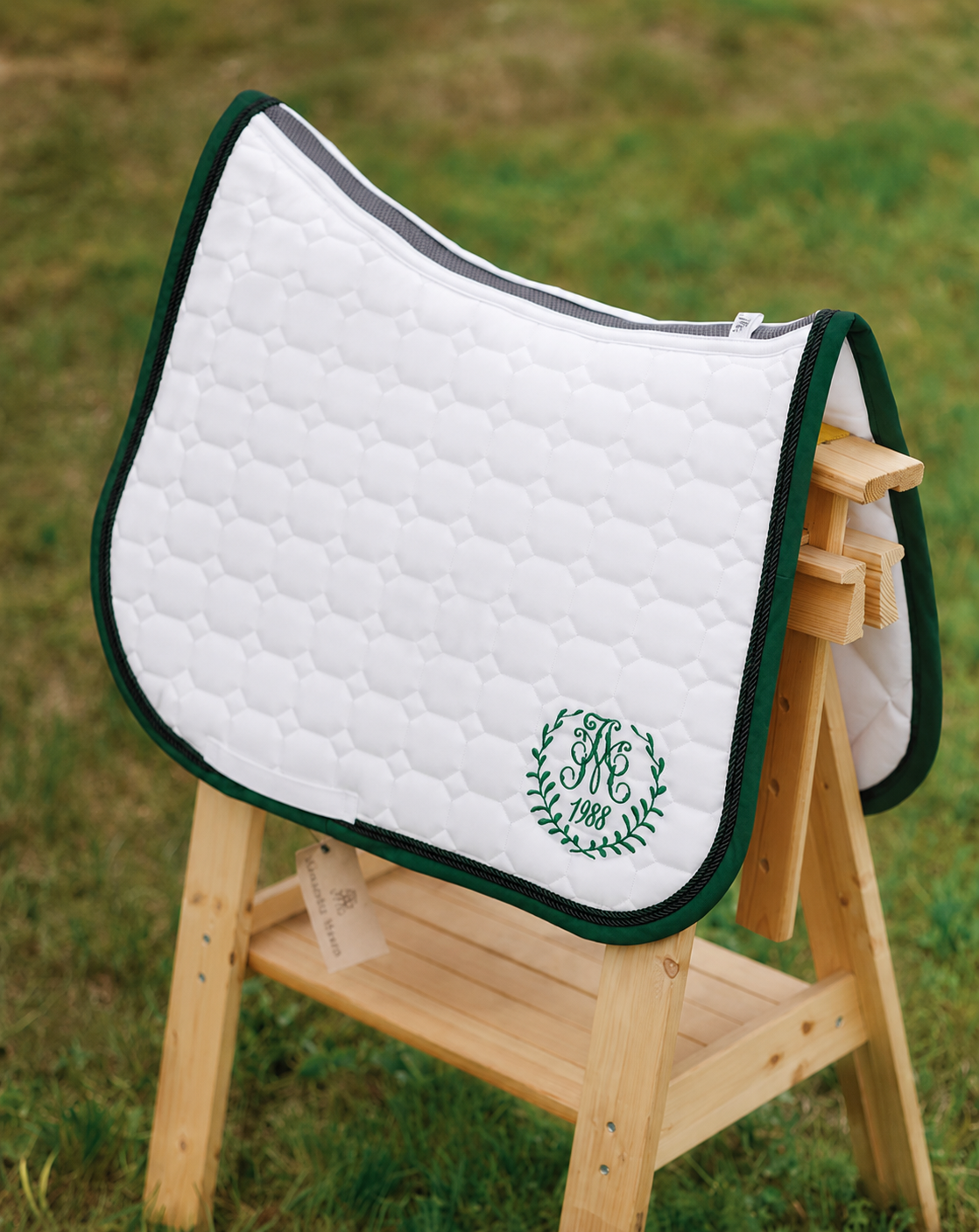 White quilted dressage saddle pad with green trim and monogram