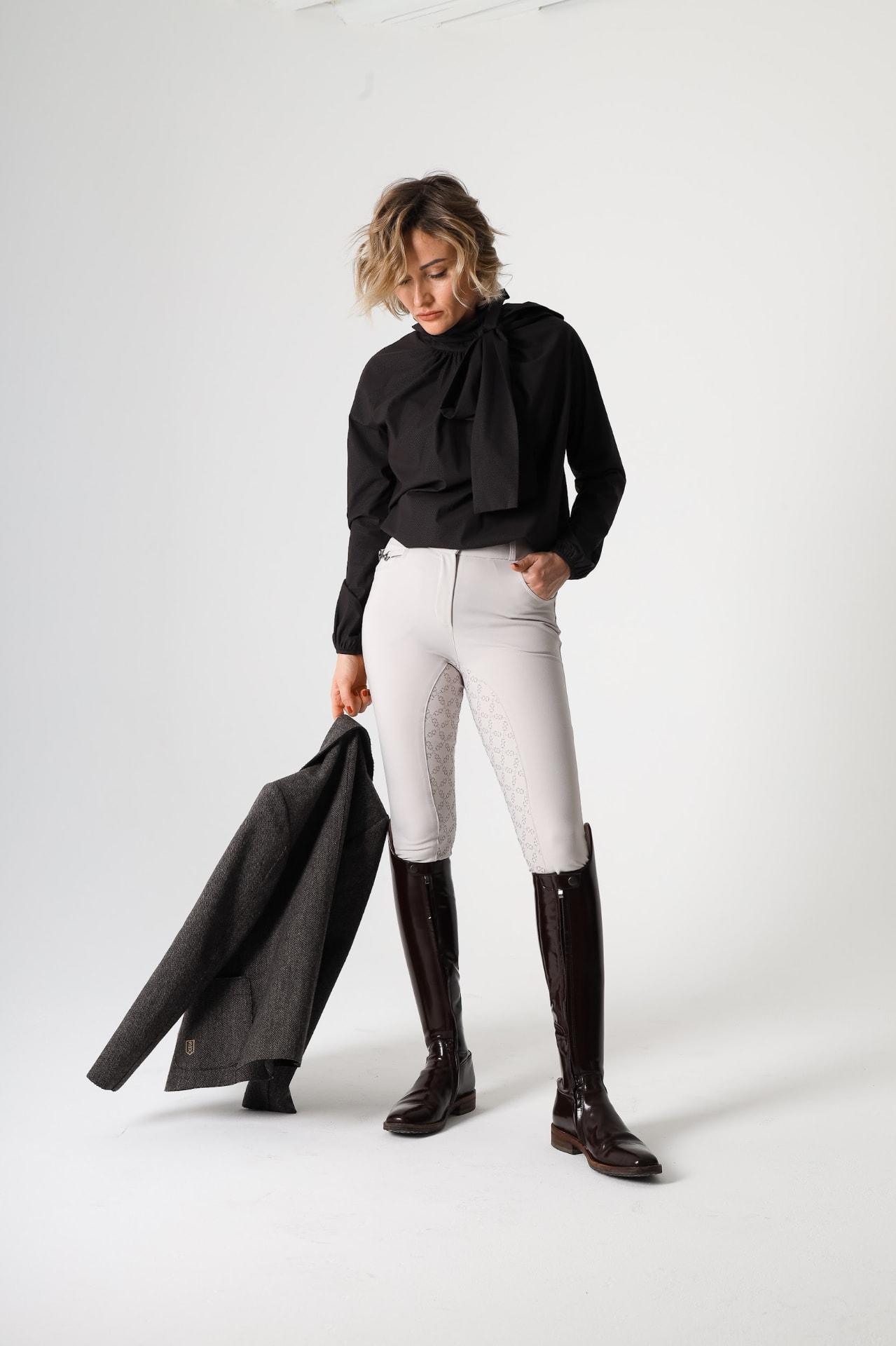 Model in a black bow-neck show shirt, pale breeches and patent boots